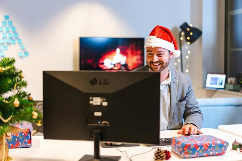 Remote worker in Santa hat receiving holiday gifts virtually.