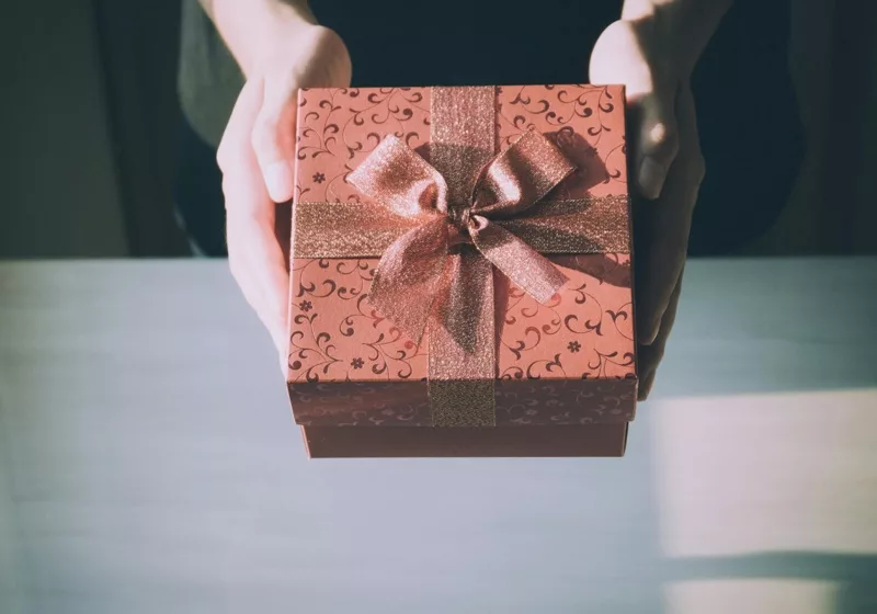 Hands holding a decorative gift box with a ribbon.