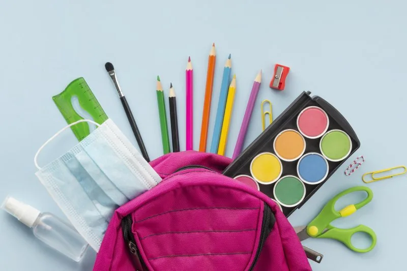 Colorful school supplies including paint, pencils, mask, and backpack
