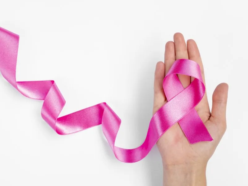 Hand holding pink ribbon symbol promoting community support through breast cancer awareness giveaways.