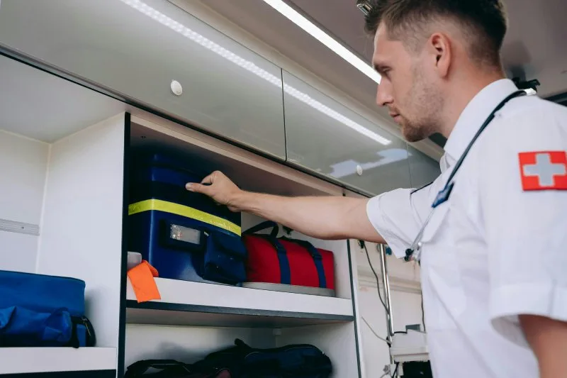 Emergency medical professional retrieving gear bag from ambulance storage, demonstrating workplace safety preparedness and emergency essentials.