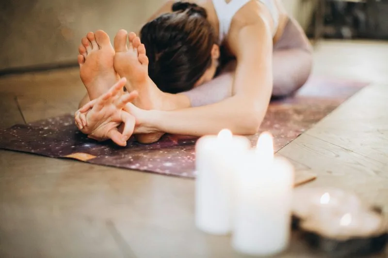 Woman stretching on yoga mat near glowing candles, representing fitness and relaxation employee wellness gifts.