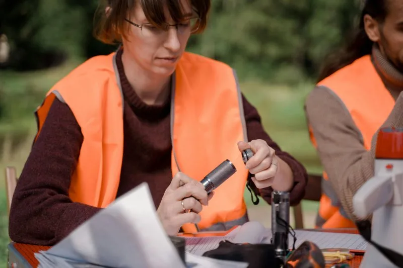 Woman in orange safety vest assembling flashlight, showcasing safety tools and gear as thoughtful promotional gifts.