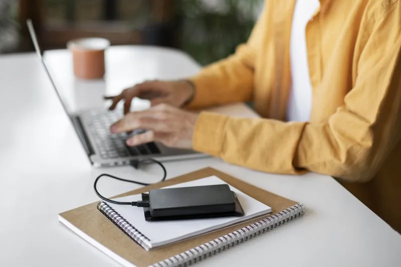 Person working on laptop with external power bank, demonstrating tech and communication safety gift ideas for employees.