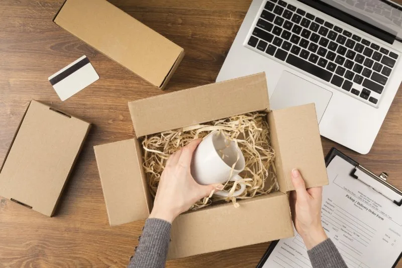  Person packing a branded mug in a shipping box, representing custom merch fulfillment.