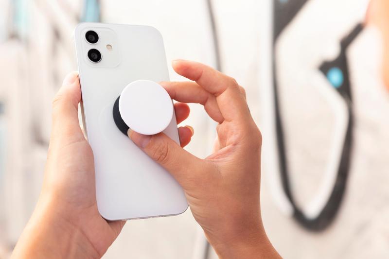 Hands attaching a white PopSocket to the back of a white smartphone.