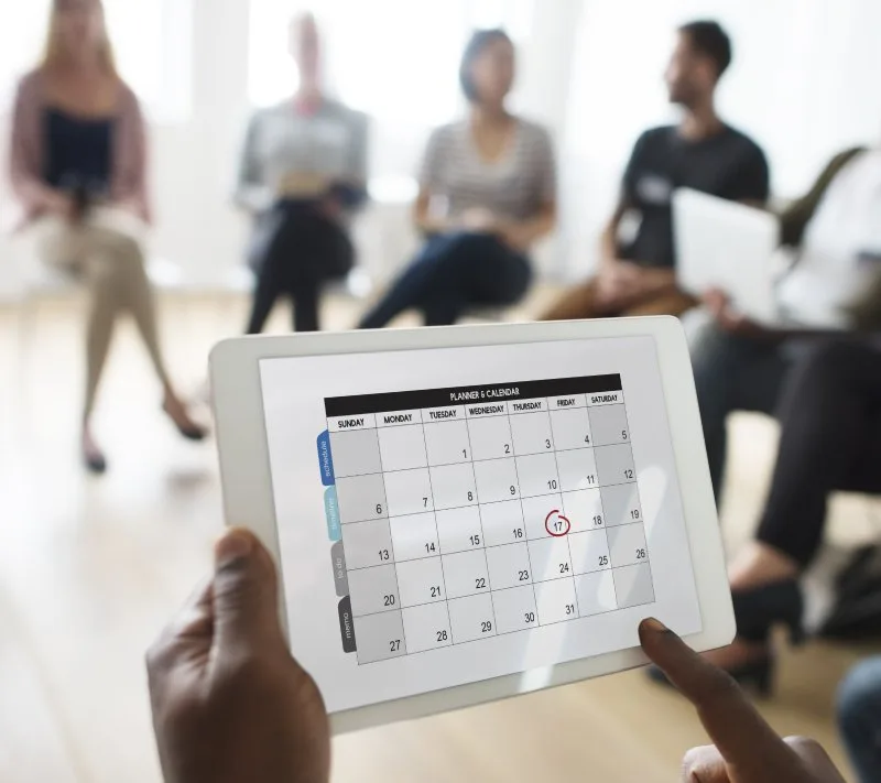 Person holding tablet with calendar during trade show planning, highlighting the importance of maximizing networking schedules effectively.
