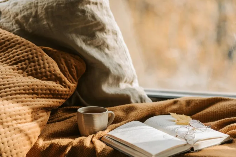 Cozy fall setting with coffee, open book, and blanket inspiring seasonal Thanksgiving giveaway ideas.