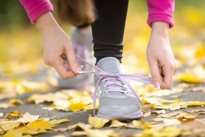Runner tying shoelaces on autumn leaves path, showcasing Thanksgiving 5K giveaway ideas with branded gear.