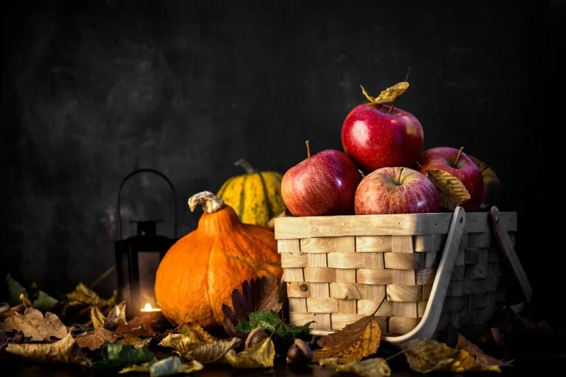 Basket with apples, pumpkins, lantern, and leaves highlighting Thanksgiving basket giveaway ideas for families.