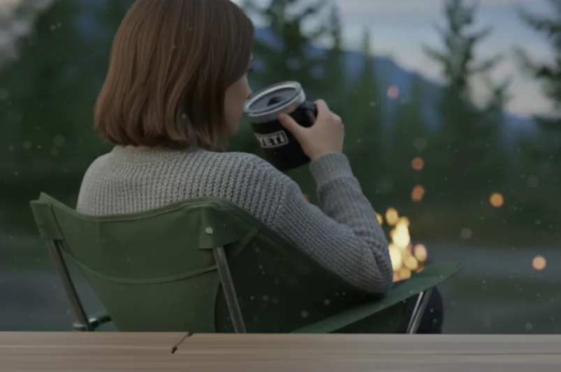 Camper sitting in a chair by the fire, drinking out of a YETI mug.