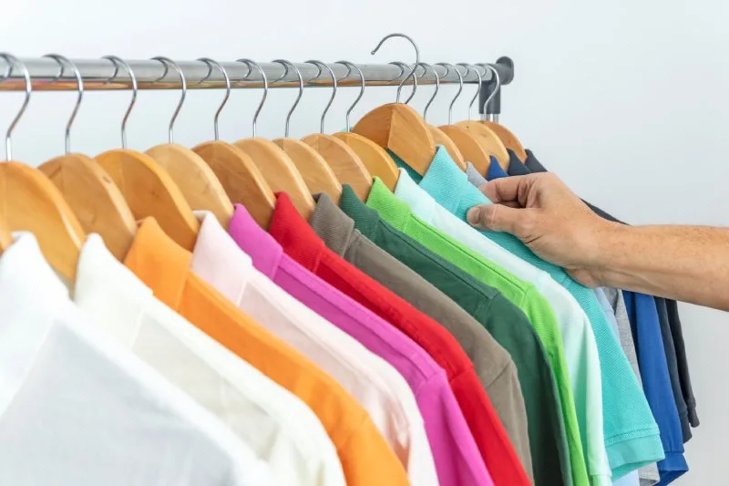 Hand selecting a turquoise polo shirt from wooden hangers, showing a variety of colorful polo shirt options for corporate uniforms