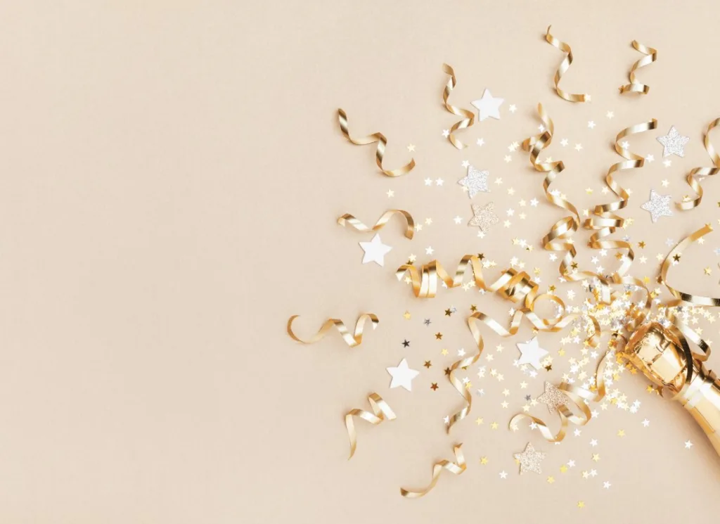 New Year party decorations with gold streamers, white stars and glitter confetti on neutral background