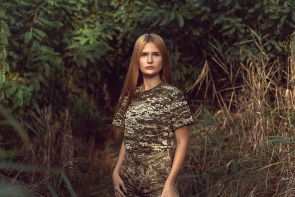 Woman wearing custom camo shirts and tactical pants standing in a dense green forest.