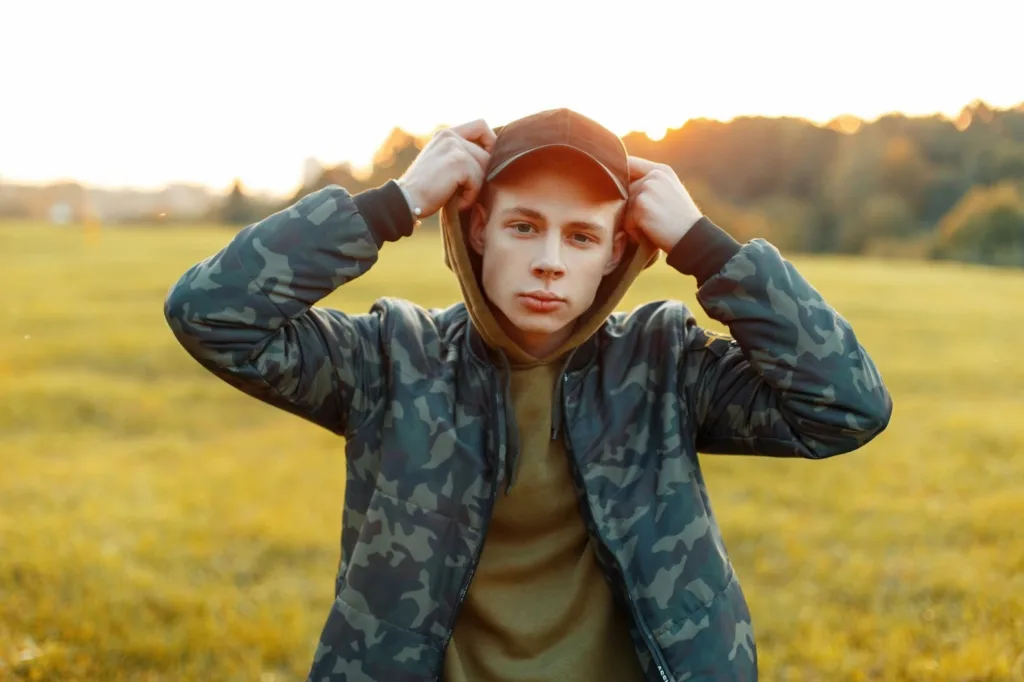 Man wearing custom camo hoodies and a baseball cap in a field during sunset.