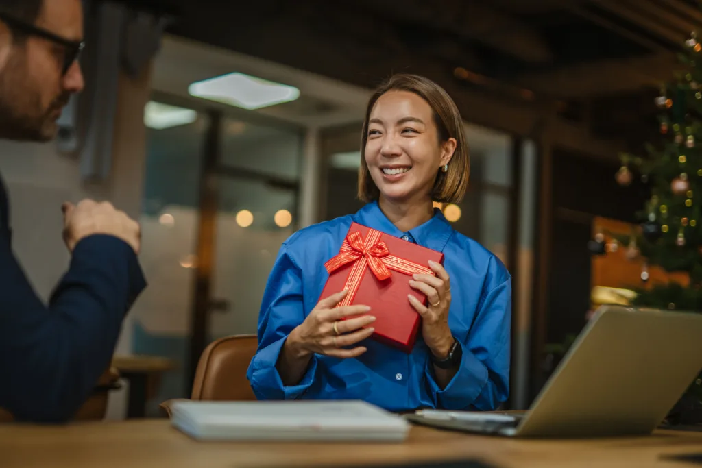 Woman smiling brightly and holding a wrapped red appreciation gift for employees