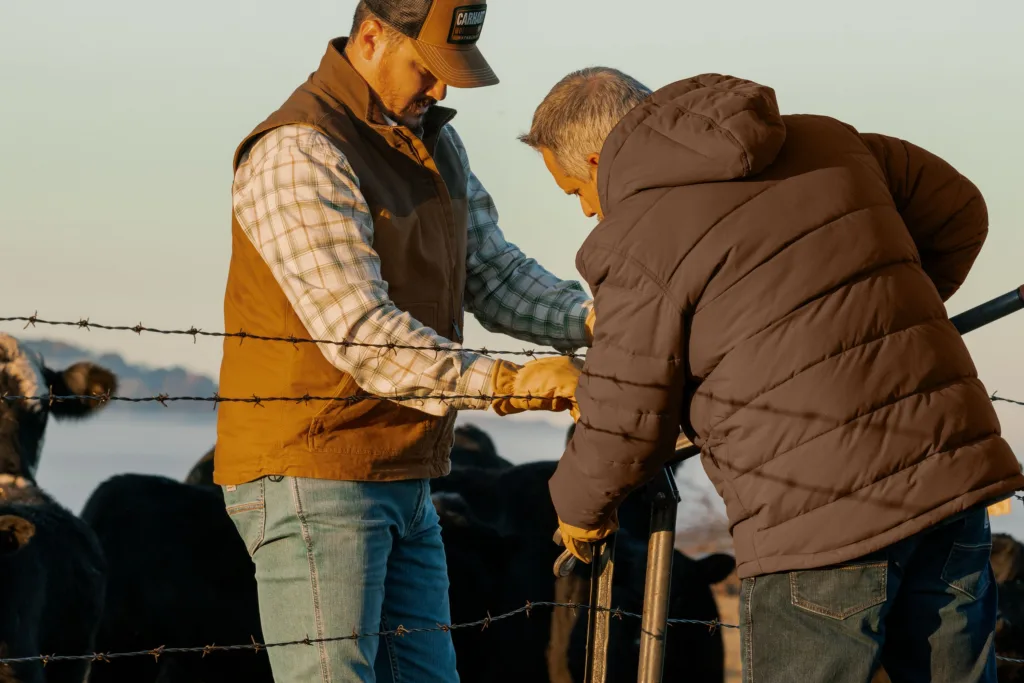 Two men in Carhartt company gear repairing a fence.