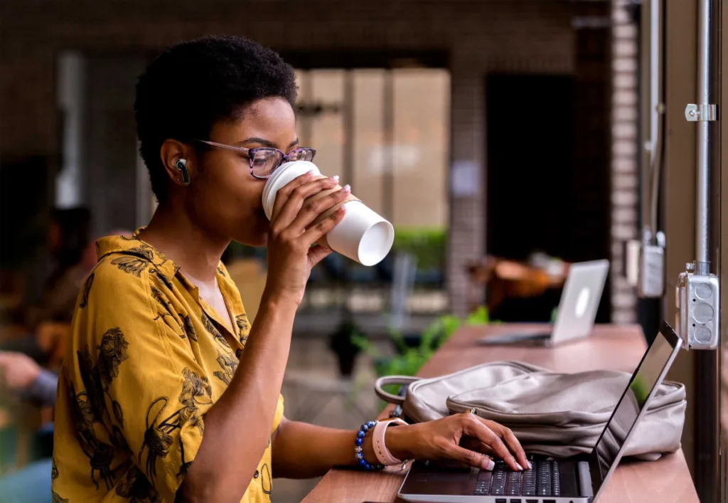 Woman drinking coffee wearing branded wireless earbuds for executive leadership retreats