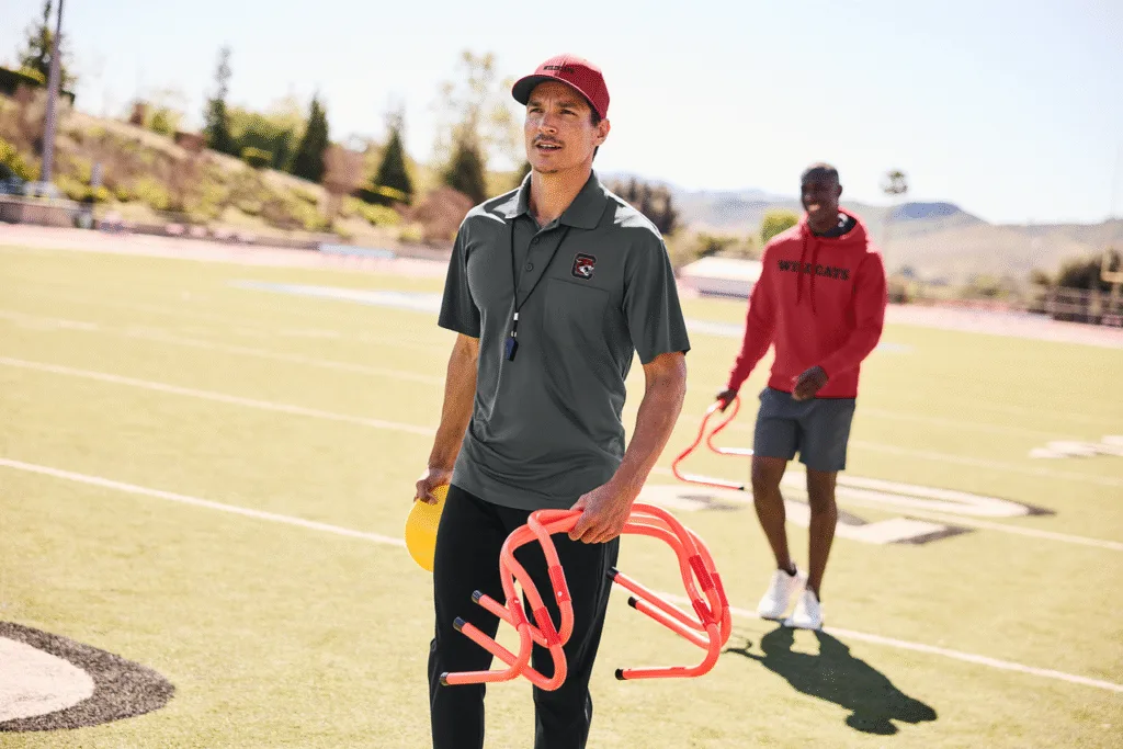 Two football coaches on field wearing staff shirts