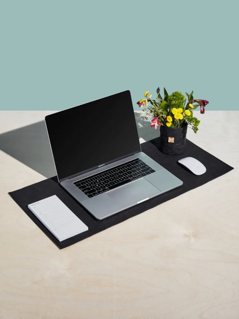 Laptop with mouse and flowers on top of branded desk mat