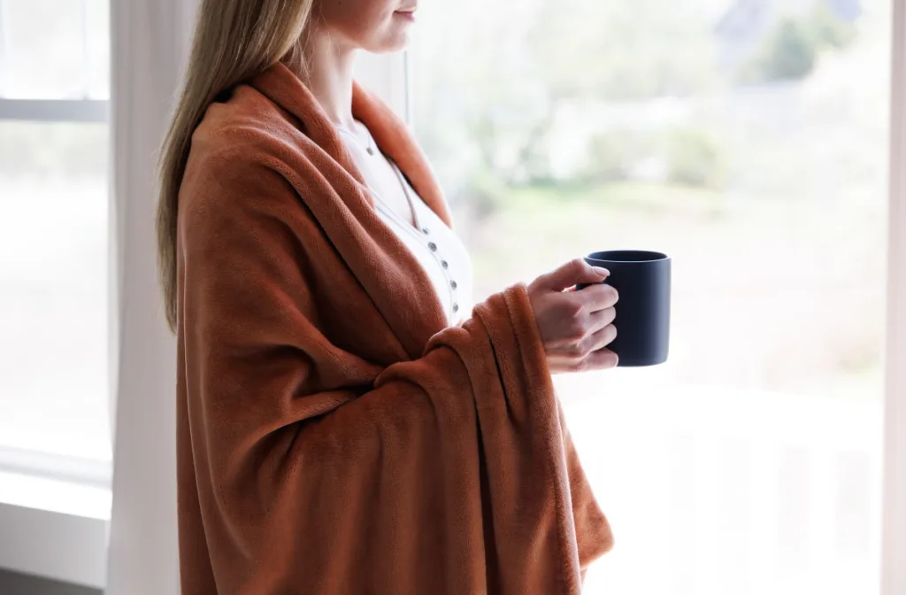 Woman in orange blanket holding a mug