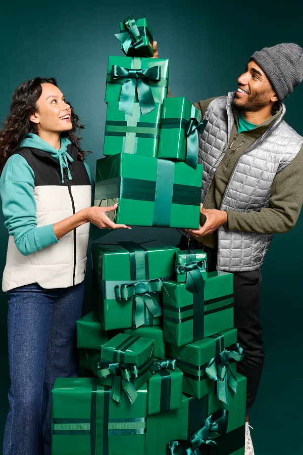 A man and a woman stacking gifts wrapped in green paper while wearing The North Face jackets