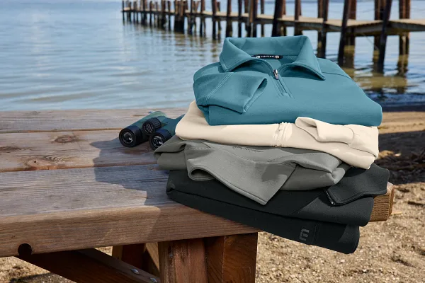 TravisMathew pullovers stacked in front of lake